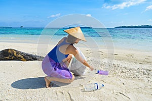 Woman collecting plastic bottles on beautiful tropical beach, turquoise sea, sunny day, recycling rubbish concept, environmental