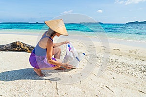 Woman collecting plastic bottles on beautiful tropical beach, turquoise sea, sunny day, recycling rubbish concept, environmental