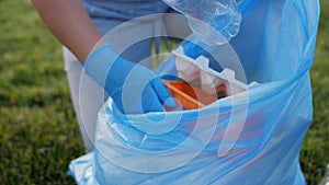 A woman collects garbage in a park in a blue garbage bag, close-up.