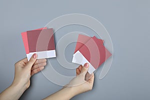 Woman with color sample cards choosing paint shade near grey wall, closeup. Interior design