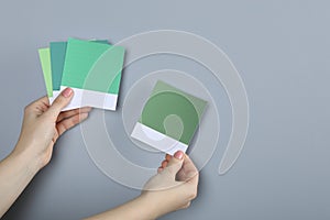 Woman with color sample cards choosing paint shade near grey wall, closeup. Interior design