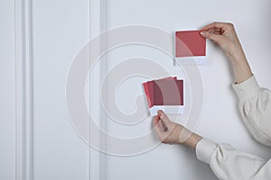 Woman with color sample cards choosing paint shade near white wall, closeup. Interior design