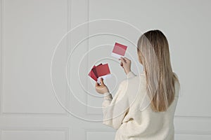 Woman with color sample cards choosing paint shade for wall indoors, back view. Interior design