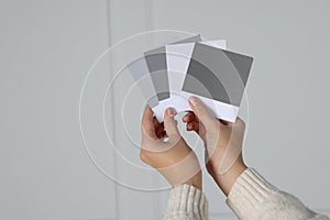 Woman with color sample cards choosing paint shade for wall indoors, closeup. Interior design