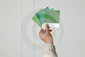 Woman with color sample cards choosing paint shade for wall indoors, closeup. Interior design