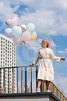 A woman with colored hair with an armful of balloons against a blue sky. Vertical photo.