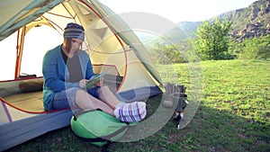 Woman in colorful socks and kerchief sits in a tent and looks on map in her hands under sunlight.