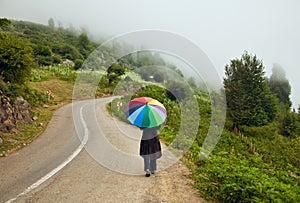 Woman with Colorful Umbrella Walking down a Foggy Winding Road