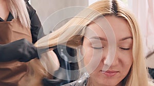 Woman combing beautiful blonde hair of a client in a hairdressing salon.