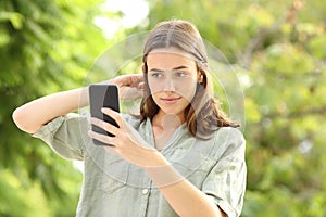 Woman combing hair using smartphone as a mirror