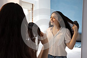 Woman combing her hair and smiling in front of the mirror