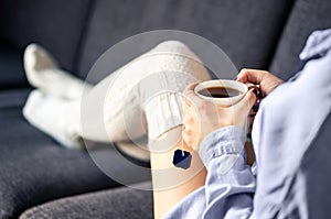 Woman in comfy warm socks drinking cup of tea in winter. Home comfort and relaxed morning on weekend. Trendy fashion style.
