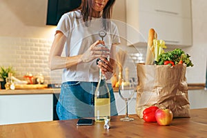 Woman coming home with grocery bags and opening bottle of white wine