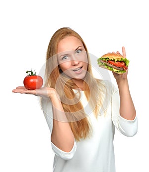 Woman comparing tasty unhealthy burger sandwich in hand and tomato