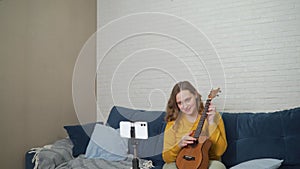 Woman conducts an online lesson and teaches students to play the ukulele. Holds guitar in hands and tells people about