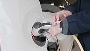 Woman connecting power supply to electric vehicle for charging and blocks car using smart watch.