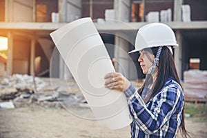 Woman construction engineer hold blueprint wear plaid shirt safety white hard hat at construction site industry labor worker.