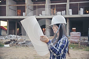 Woman construction engineer hold blueprint wear plaid shirt safety white hard hat at construction site industry labor worker.