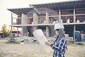 Woman construction engineer hold blueprint wear plaid shirt safety white hard hat at construction site industry labor worker.