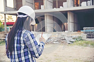 Woman construction engineer writing note wear plaid shirt safety white hard hat at construction site industry labor worker.