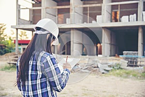 Woman construction engineer writing note wear plaid shirt safety white hard hat at construction site industry labor worker.