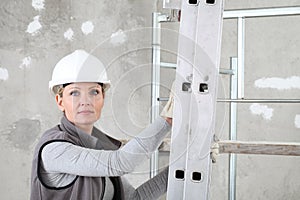 Woman construction worker builder portrait wearing white helmet holding a ladder on  interior site building background with