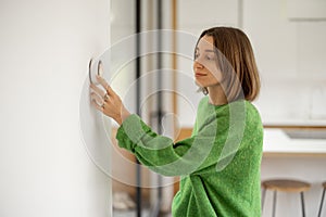 Woman controlling temperature with a smart thermostat at modern apartment.