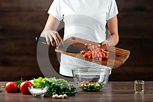 Woman cook cuts vegetables for salad preparation on a wooden background. Proper healthy eating