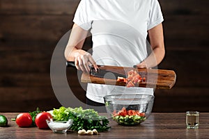 Woman cook cuts vegetables for salad preparation on a wooden background. Proper healthy eating