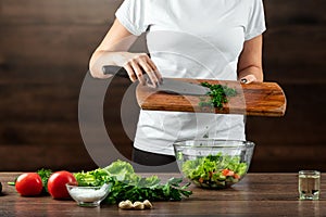 Woman cook cuts vegetables for salad preparation on a wooden background. Proper healthy eating