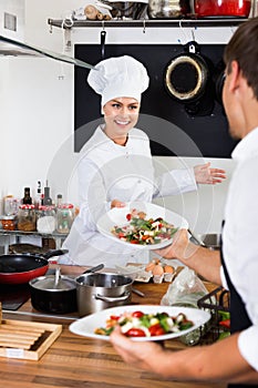 Woman cook giving to waitress ready to serve salad