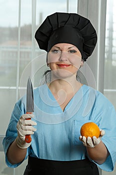 The woman cook holds an orange in her hand and in the other hand a knife.