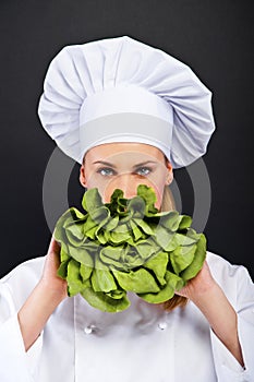 Woman cook with lettuce in her hand standing on black background