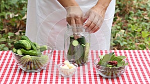 Woman cook puts cucumbers and spices in a glass jar for preservation