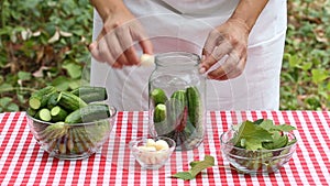 Woman cook puts cucumbers and spices in glass jar for preservation