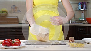 Woman cook throws dough in her hands. Preparation of pizza dough. Woman in yellow clothes and tomatoes on the table.