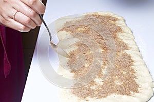 A woman is cooking buns with cinnamon. She rolls the stuffing onto the rolled dough. Mixed sugar and cinnamon.