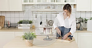 Woman is cooking cakes. She is cutting figs and decorating a cake or cheesecake. White kitchen in the background.