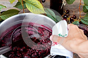 Woman is cooking cherry jam  and is bottling it in to the jars