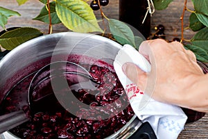 Woman is cooking cherry jam  and is bottling it in to the jars
