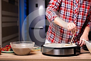 Woman cooking delicious crepe on electric pancake maker in kitchen, closeup