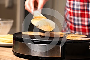 Woman cooking delicious crepe on electric pancake maker in kitchen, closeup