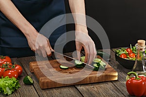 Woman cooking fresh healthy salad. Female hands cutting vegetables on board on wooden table with copyspace.