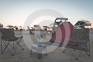 Woman cooking with gas stove in camping site at dusk. Gas burner, pot and smoke from boiling water, tent in the background. Advent