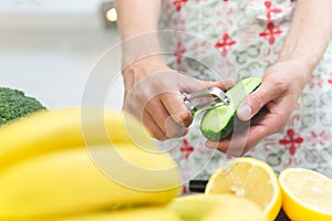 Woman cooking healthy food in her kitchen, she is peeling a fresh cucumber on the chopping board