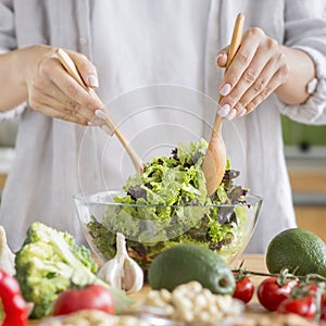 Woman cooking healthy food in the kitchen and mixing fresh salad