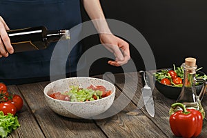 Woman cooking healthy food on wooden table with copyspace. Female hands adding olive oil into bowl with vegetable salad.