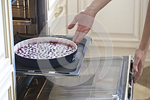 Woman cooking in the kitchen, puts cakes in the oven. preparation of a French pie with cherries. Clafoutis cherry pie.