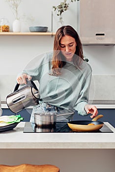 Woman cooking a meal at home, pours water into a pot from a kettle