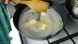 Woman cooking melting butter cubes on frying pan mixing with wooden spatula.